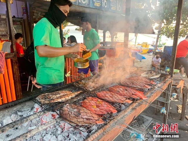 印尼巴厘岛著名旅游景点金巴兰海滩烤鱼摊员工为游客烤鱼